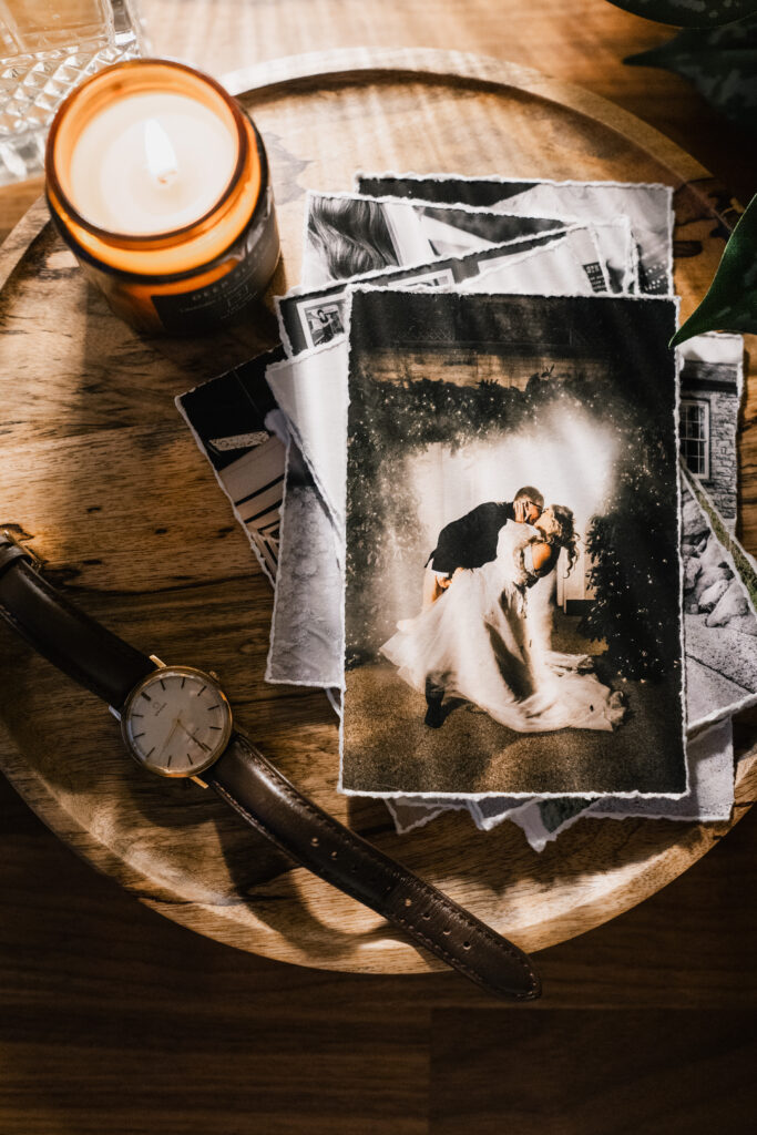 A wooden tray with a lit candle, a wristwatch, and a stack of black-and-white photos; the top photo shows a couple in wedding attire sharing a kiss.